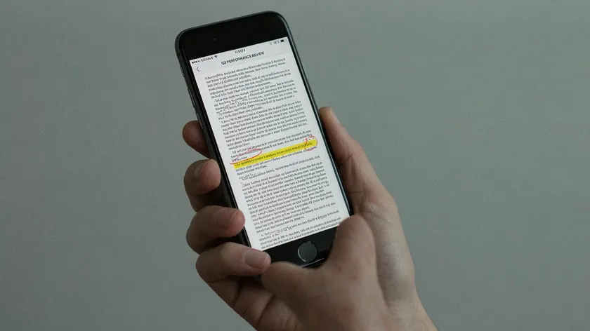 Hand holding an iPhone showing a PDF page with a yellow highlight and red pen marks